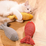 Cat playing with a yellow and orange Catnip Fish Plush Toy on a wooden floor with two fish-shaped toys nearby.