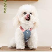 White dog wearing Cute Pet Overalls Dress Denim and Plaid Style a red checkered harness and blue vest on a wooden floor.