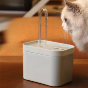 Cat drinking water from a white Modern Pet Water Fountain  on a wooden surface.