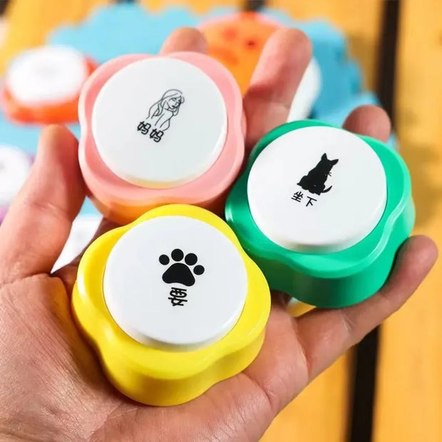 Four colorful Pet Training Button with different symbols held in a hand against a blurred background