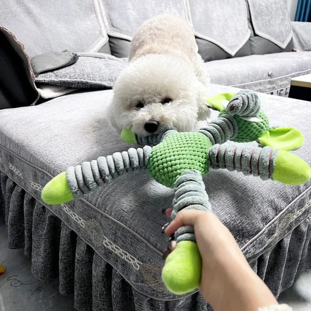 White dog playing with a green and gray Plush Animal Dog Toys on a gray couch.