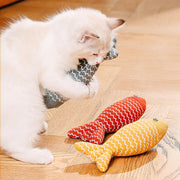 White cat playing with a red and yellow Catnip Fish Plush Toy on a wooden floor.