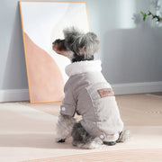 Small dog wearing a gray Corduroy Dog coat with a pink patch, standing on a light-colored floor.