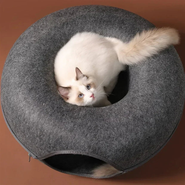Cat inside a gray donut-shaped Felt Cat Cave Bed on a brown background
