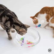 Two cats interacting with a clear bowl containing colorful Interactive Electric Swimming Fish Toys on a white background