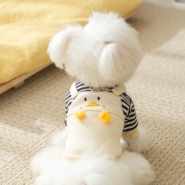 White fluffy dog wearing a striped Duck Overalls Pet Outfit on a beige surface.