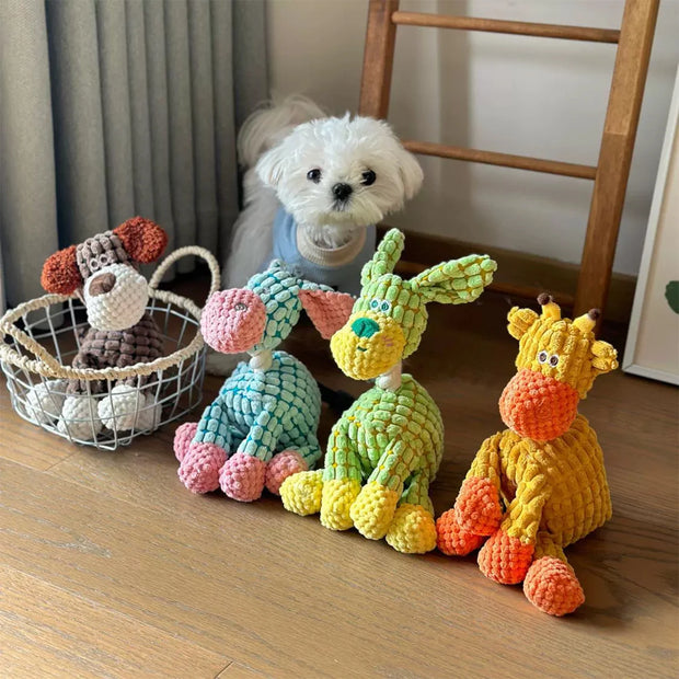Colorful knitted Plush Animal Rope Dog Toys on a wooden floor with a small white dog sitting behind them.