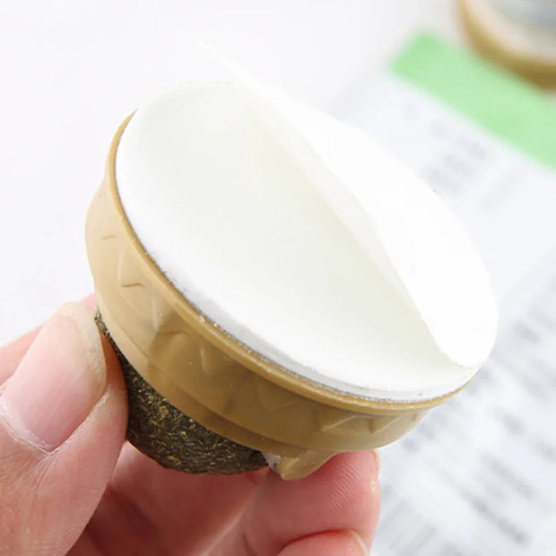 Round object with textured base held by a Catnip Ball Toy and hand against a blurred background