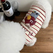 Dog wearing a Striped Bear T-Shirt with cartoon design on a wooden floor next to a bottle of wine and glasses.