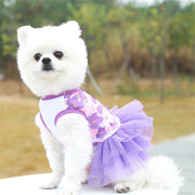 Small white dog wearing a purple and pink Adorable Floral Dog Dress in an outdoor setting.
