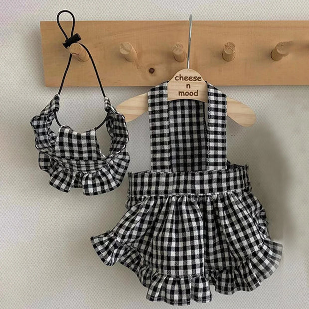 Black and white Checkered Pet Dress with Matching Bib with matching headband on a wooden hanger against a neutral background.