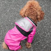 Small dog wearing a pink Dog Raincoat with Clear Hood on a gray pavement.