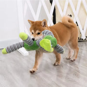 Dog playing with a green and gray Plush Animal Dog Toys on a light wooden floor.
