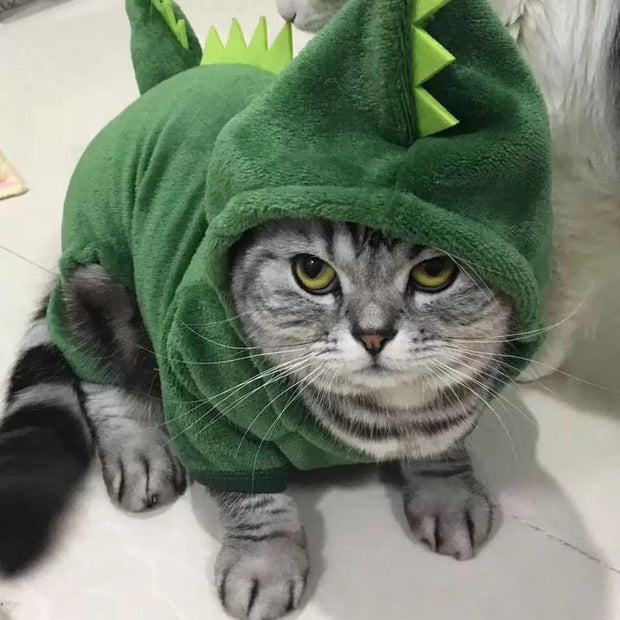 Cat wearing a green Dinosaur Hoodie Costume on a light-colored floor.