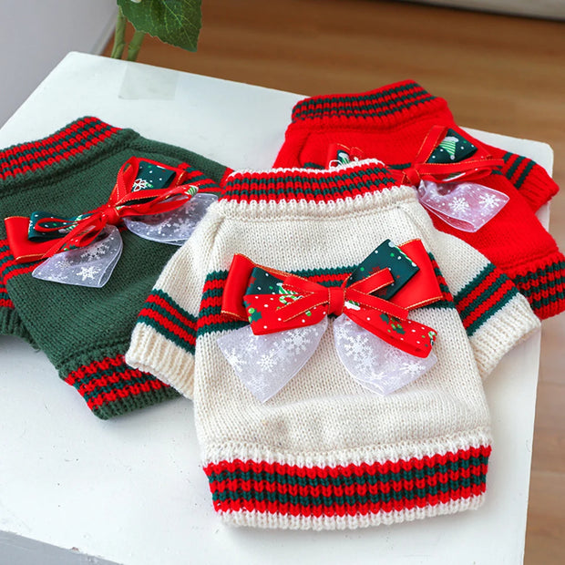 Three knitted Christmas Dog Sweater in red, green, and white with decorative bows on a white surface.
