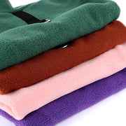 Stack of folded Fleece Dog Jacket fabric in green, brown, pink, and purple on a white background