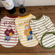 Three dog Striped Bear T-Shirt with cartoon bear designs on a wooden surface, one of which is a Montes wine bottle.