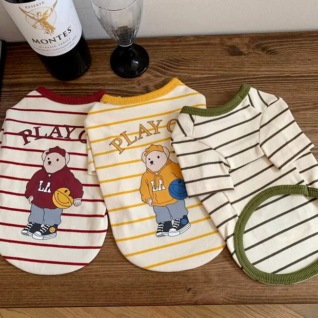 Three dog Striped Bear T-Shirt with cartoon bear designs on a wooden surface, one of which is a Montes wine bottle.