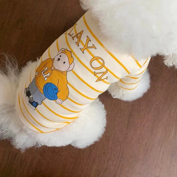 White dog wearing a yellow and white Striped Bear T-Shirt with a cartoon character on a wooden floor.