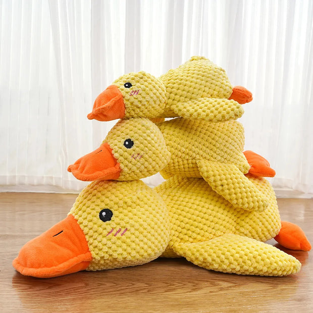 Three yellow and orange Dog Calming Duck Plush Toy on a soft surface
